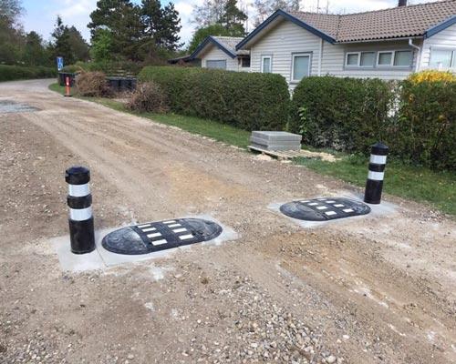 TDJ Vejbump 30 km/t med pullert fra Trafikgummi.dk. Typegodkendt af vejdirektoratet. Monteret på grusvej ovenpå fliser. TDJ Vejbump 30 km/t med pullert fra Trafikgummi.dk. Typegodkendt af vejdirektoratet. Monteret på grusvej ovenpå fliser.