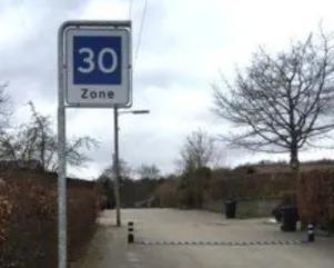 Tydeligt 30-zone trafikskilt monteret på robust stander ved et TDJ pudebump i gummi på en offentlig vej. Tydeligt 30-zone trafikskilt monteret på robust stander ved et TDJ pudebump i gummi på en offentlig vej.